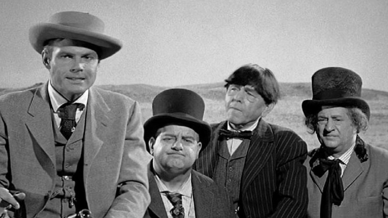 Kenneth Cabot and the Three Stooges, on a horse-drawn cart, facing the camera. The Stooges look confused. A scene from The Outlaws Is Coming.