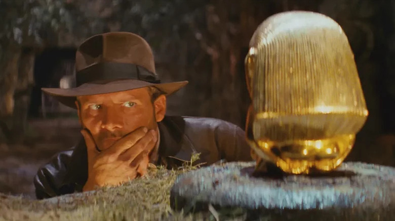 Indiana Jones (Harrison Ford) rubs his chin while examining a golden idol in Raiders of the Lost Ark