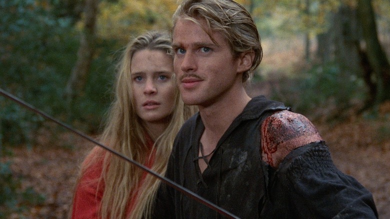 Buttercup (Robin Wright) stands behind Westley (Cary Elwes) as he holds a sword in a forest in The Princess Bride