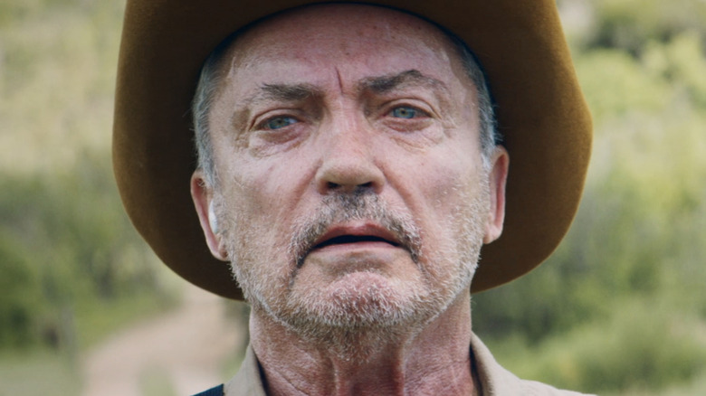 Udo Kier as Michael is seen in closeup against a green background in Bacurau