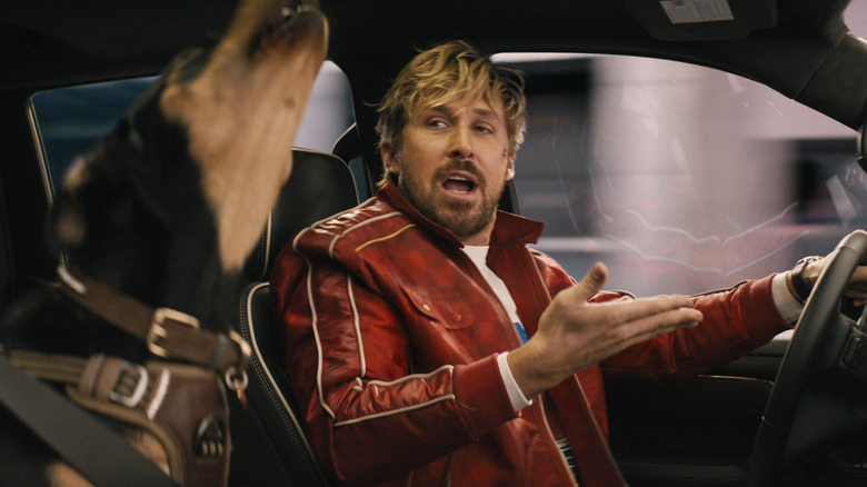Ryan Gosling as Colt Savers driving a car with a howling dog and riding shotgun in The Fall Guy