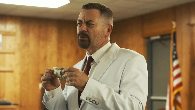 Nick Offerman's Jerry Kane holds up a dollar bill as he stands in an office in Sovereign