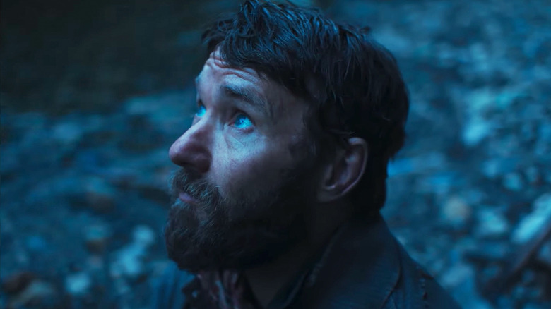 Joel Edgerton as Robert Grainier looks up at the sky while he kneels outside in Train Dreams