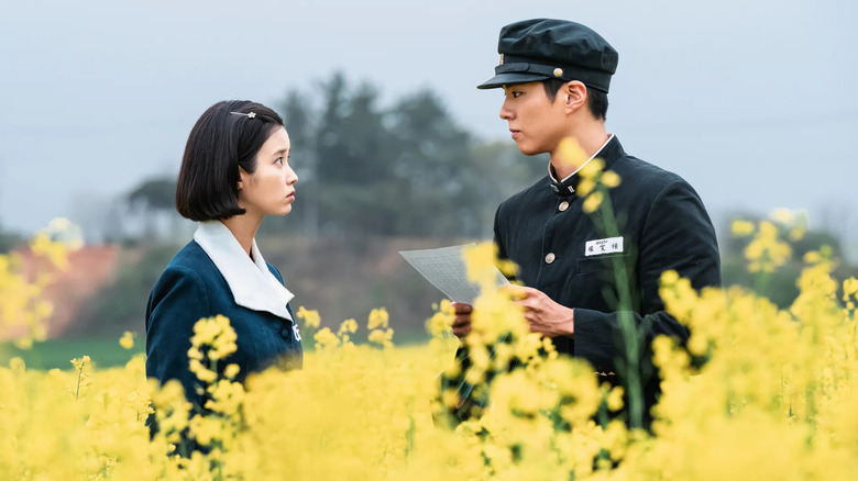 Oh Ae-sun (IU) and Yang Gwan-sik (Park Bo-gum) look at each other in a flowery field while wearing school uniforms in When Life Gives You Tangerines