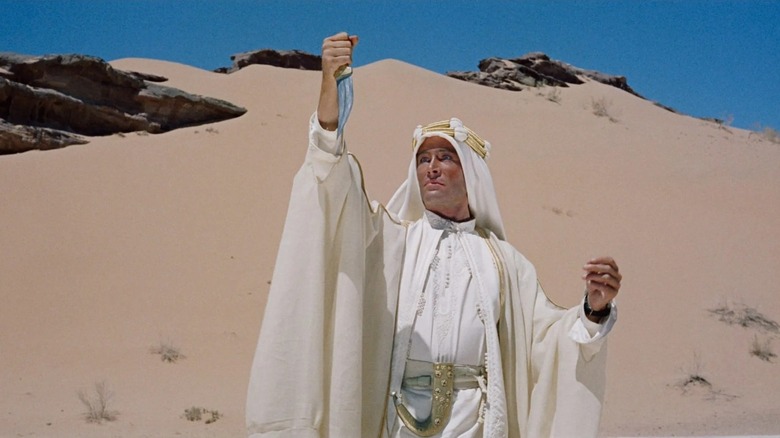 T.E. Lawrence (Peter O'Toole) stands in the desert, holding a dagger in his right hand and looking at it intensely in Lawrence of Arabia