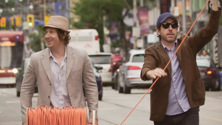 మాట్ జాన్సన్ మరియు జే మెక్‌కారోల్ నిర్వణ్ణ ది బ్యాండ్ ది షో ది మూవీలో టొరంటో వీధుల్లో పొడవైన పొడిగింపు త్రాడును లాగుతున్నారు