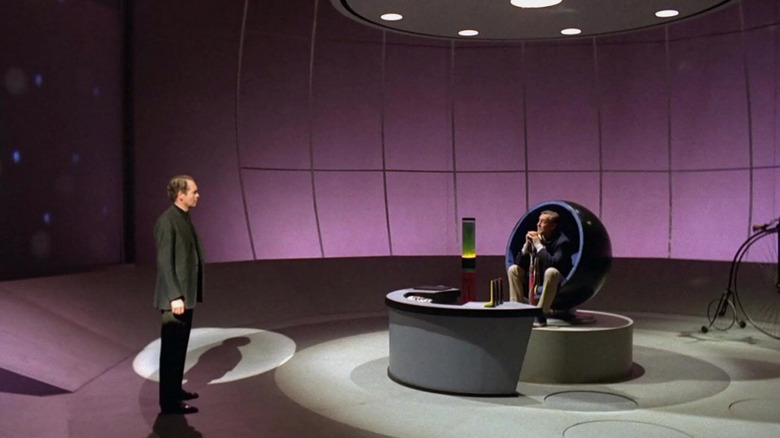Number Six talking to Number Two in a chair on a weird purple room on The Prisoner