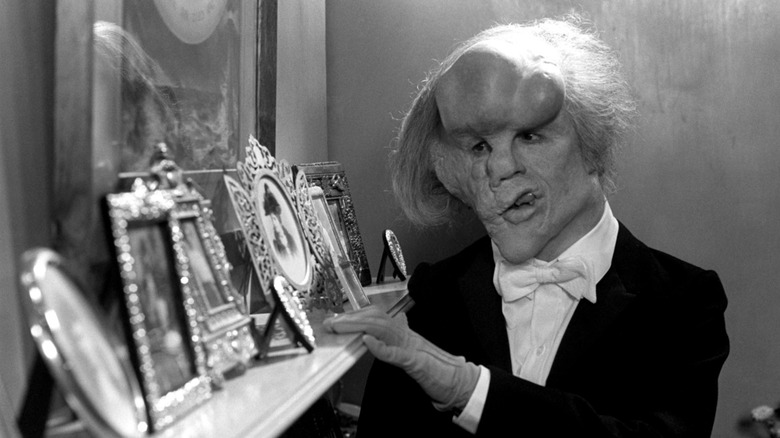 ది ఎలిఫెంట్ మ్యాన్ - తక్సేడోలో మెరిక్ ఫ్రేమ్డ్ చిత్రాలను చూస్తున్నాడు