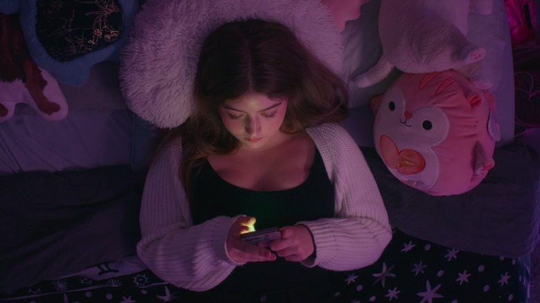 Claire Rock Smith scrolling on a phone in bed in Bad Influence