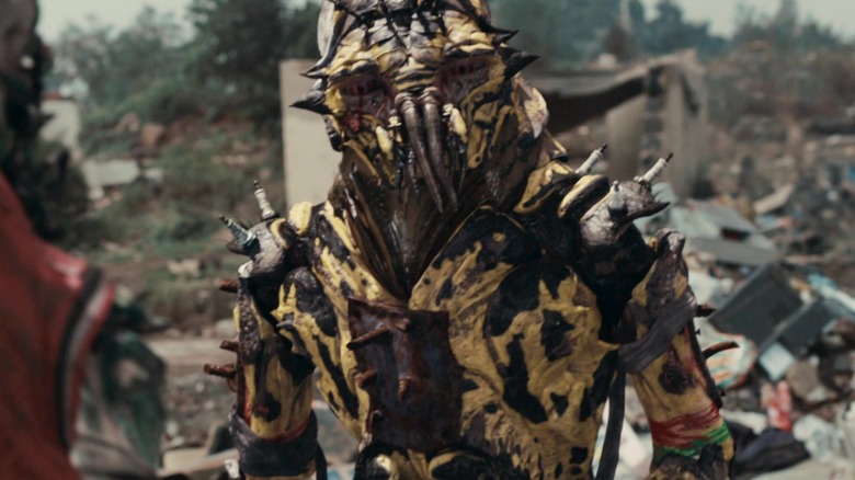 Jason Cope as an alien walking around a junkyard in District 9