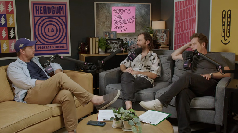 Tim Heidekcer sits on a couch opposite Kyle Mooney and Beck Bennett on the What's Our Podcast podcast
