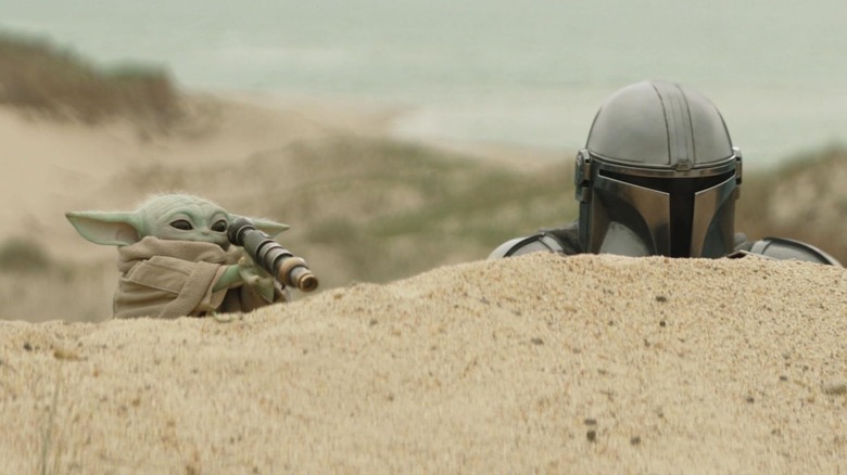 Grogu and Mando peeking over a hill in The Mandalorian and Grogu