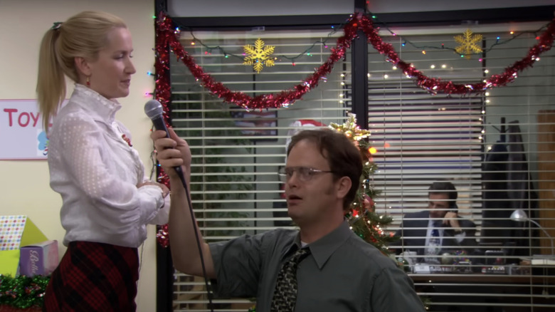 Rainn Wilson's Dwight Shrute holds a microphone for Angela Kinsey's Angela Martin to sing in The Office