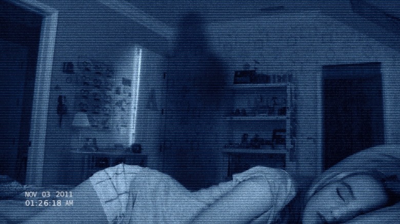 Kathryn Newton as Alex laying in bed with a ghost in the background on the poster for Paranormal Activity 4