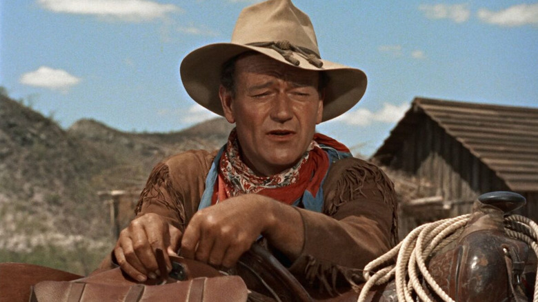John Wayne leaning against a horse saddle as Hondo Lane in Hondo