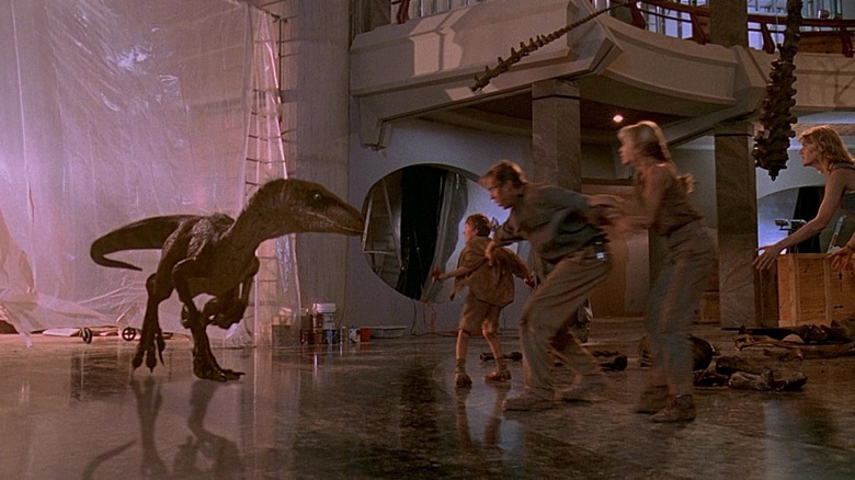 A raptor approaches Sam Neil's Doctor Alan Grant, Laura Dern's Ellie Sattler, Joseph Mazzello's Tim Murphy, and Ariana Richards' Lex Murphy at the Jurassic Park Visitor Center.