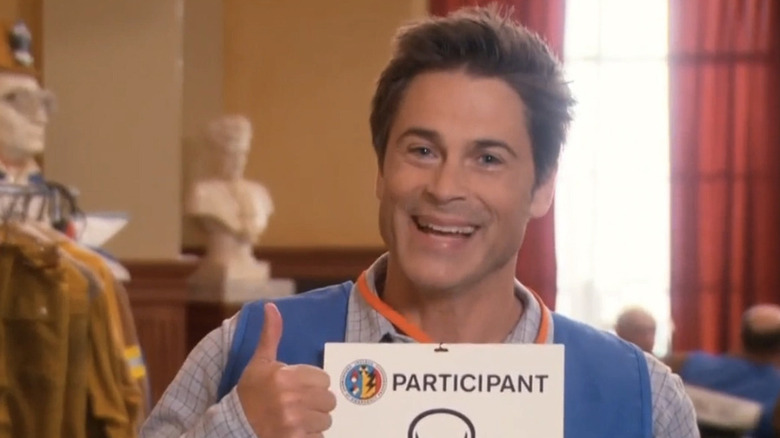 Rob Lowe as Chris Traeger giving a thumbs up and holding a participant sign on Parks and Recreation