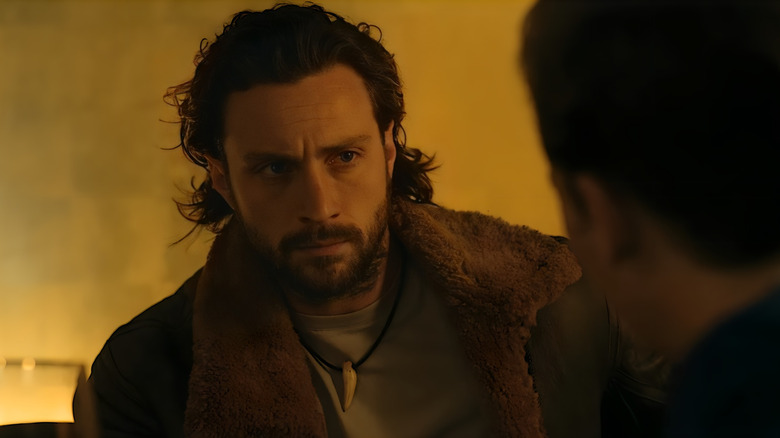 Aaron Taylor-Johnson as Kraven looking intense in front of a fire in Kraven the Hunter