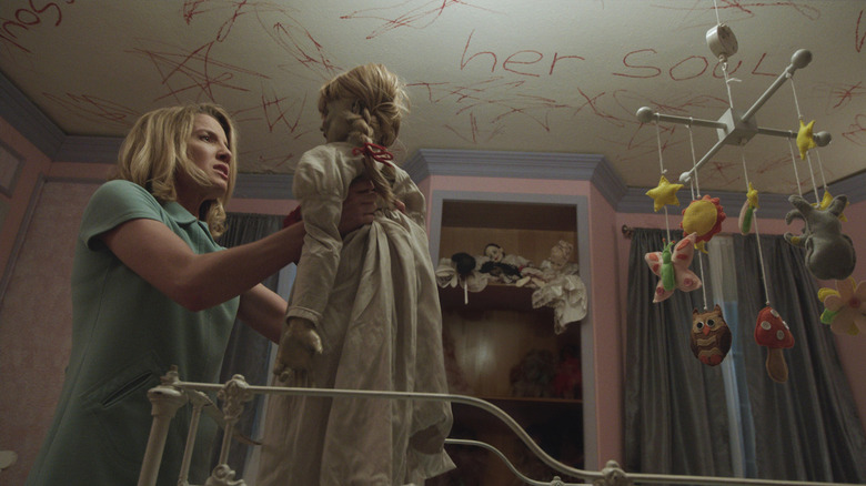 Annabelle Wallis as Mia holding the Annabelle doll with red writing on the ceiling in Annabelle