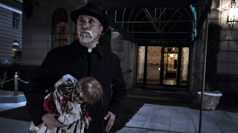 Tony Amendola as Father Perez holding the Annabelle doll outside of a building in Annabelle