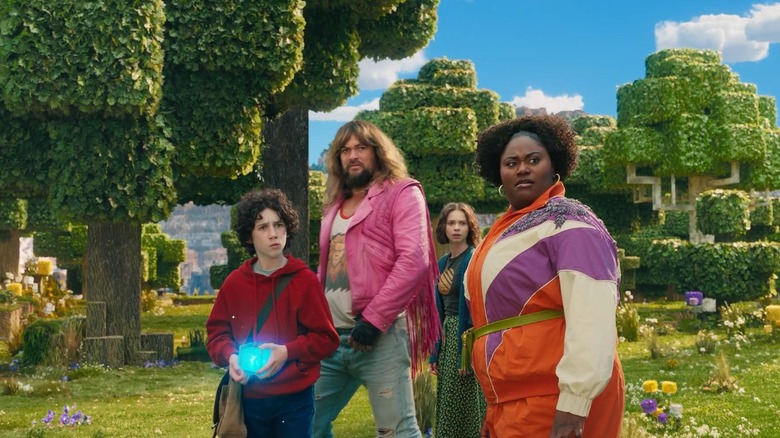 Henry, Garrett, Natalie, and Dawn, standing in a blocky Minecraft world. Henry is holding a glowing orb. A scene from A Minecraft Movie.