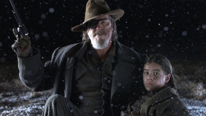 True Grit (2010) -- Rooster Cogburn holding up gun in one hand and Mattie Ross in other at night