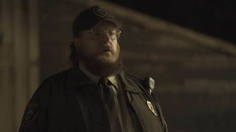 Steve Agee as John Economos wearing a security officer uniform in Peacemaker season 1