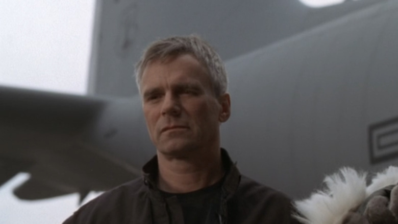 RIchard Dean Anderson is seen from a low angle standing in front of a plane in a runway in Stargate SG-1