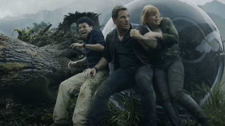 Chris Pratt's Owen Grady, Bryce Dallas Howard's Claire Dearing, and Justice Smith's Franklin Webb cower behind a fallen tree in Jurassic World: Fallen Kingdom