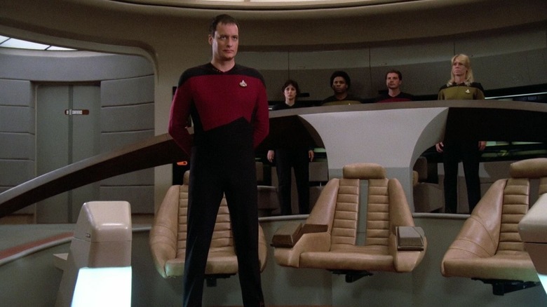 స్టార్ ట్రెక్: ది నెక్స్ట్ జనరేషన్‌లో ఎంటర్‌ప్రైజ్ యొక్క బర్డ్జ్‌పై నిరాడంబరంగా నిలబడి Q