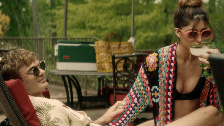 Alex Roe's Will and Andra Nechita's Cin sit outside on a sun lounger in Bone Lake