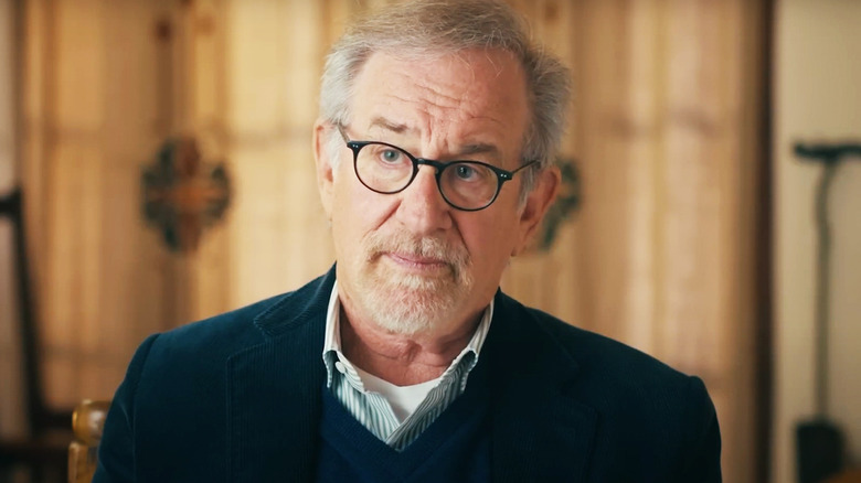 Steven Spielberg sits in a bright room for an interview in a behind the scenes featurette for The Fabelmans