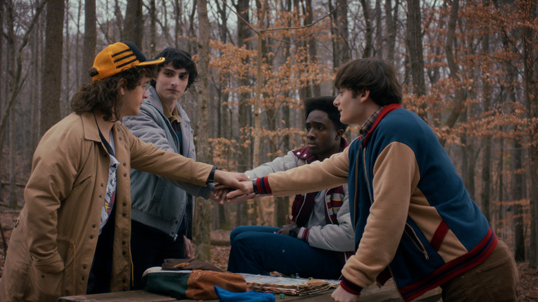 Dustin, Mike, Lucas, and Will stack hands in the middle of the woods in Stranger Things
