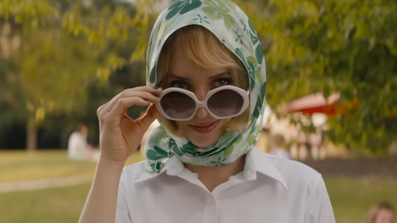 Maya Hawke as Eleanor peeking over her sunglasses and wearing a clove scarf in Do Revenge