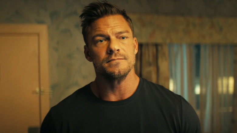 Alan Ritchson's Jack Reacher stands in a hotel room in Reacher