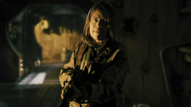 Linda Hamilton's Anya stands in an alien spaceship hallway holding a rifle in Osiris