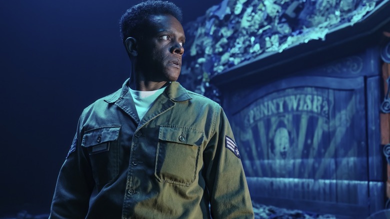 Chris Chalk as Dick Hallorann standing in front of a sign with Pennywise on it in It: Welcome to Derry