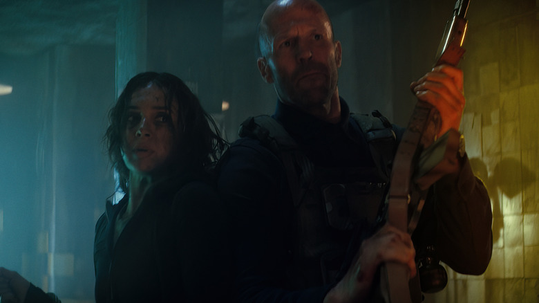 Jason Statham as Levon Cade holding a rifle and Arianna Rivas as Jenny Garcia standing behind him in A Working Man