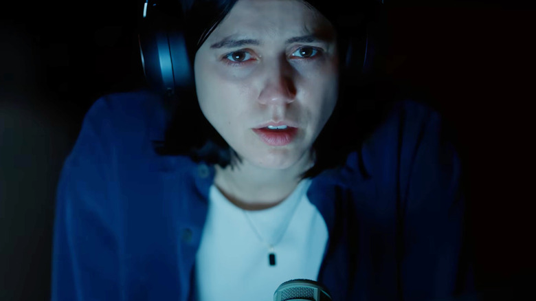Nina Kiri as Evy wearing headphones and looking scared in the dark in Undertone