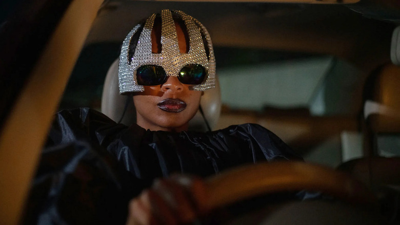 Shula in a mask driving her car in On Becoming a Guinea Fowl