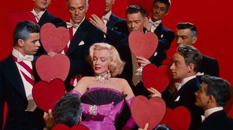 Marilyn Monroe as Lorelei in Gentlemen Prefer Blondes, wearing a pink dress and surrounded by suited dancers holding up red hearts