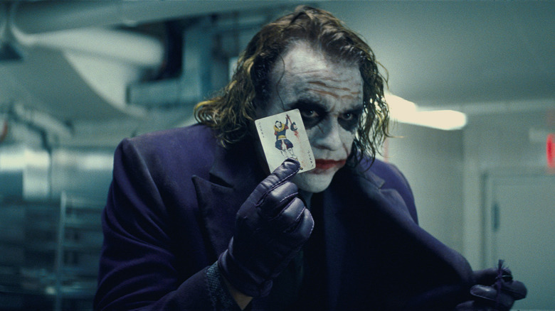 Heath Ledger as the Joker holding a Joker card in The Dark Knight