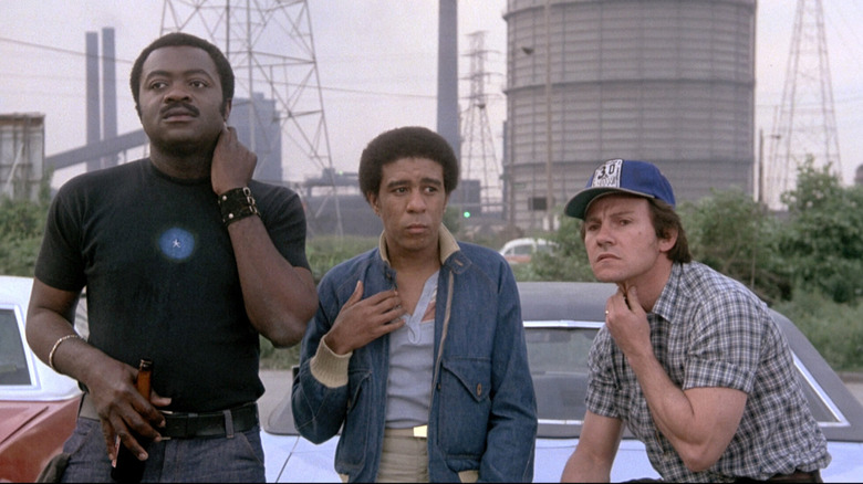 Yaphet Kotto as Sam "Smokey" James, Harvey Keitel as Jerry Bartowski, and Richard Pryor as Ezekiel "Zeke" Brown, standing against a car against an industrial background in Blue Collar