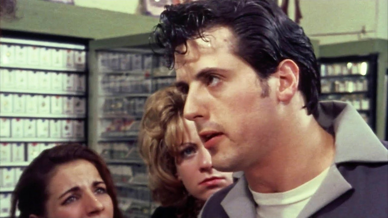 Sylvester Stallone as Stanley Rosiello in the foreground looking intensely at someone out of frame with two women looking on at him in the background in The Lords of Flatbush.