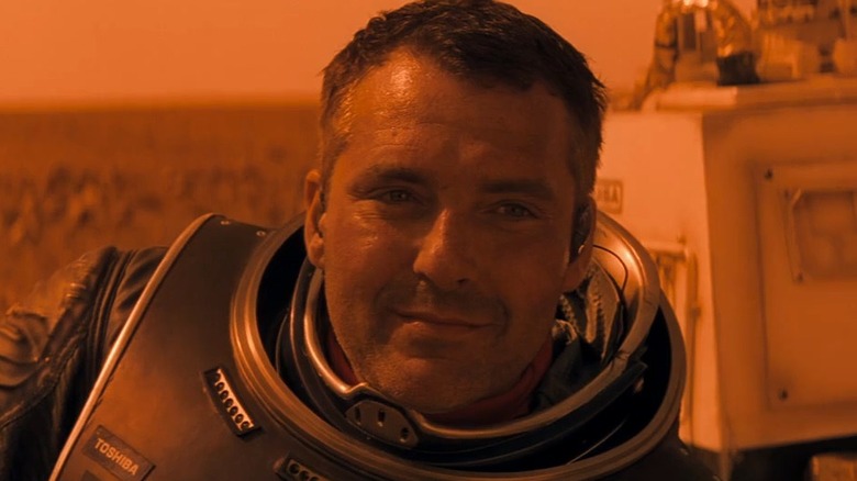 Tom Sizemore as Dr. Quinn Burchenal, softly smiling at something off-frame in Red Planet.