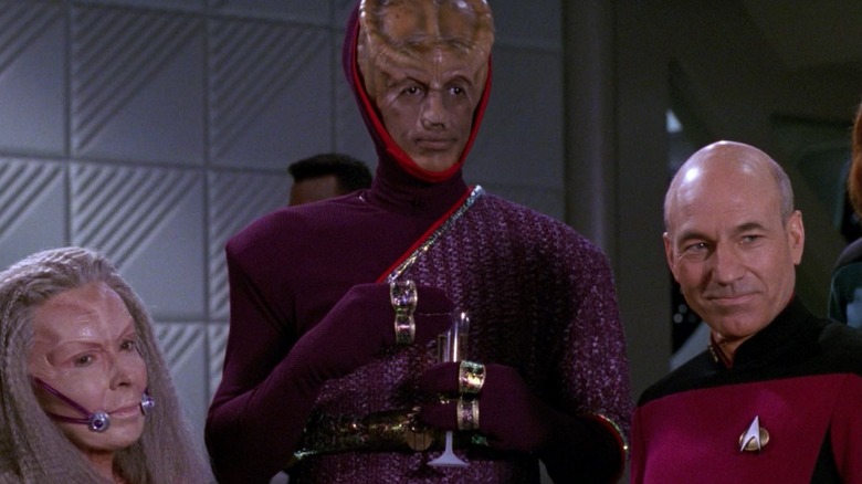 Leyor em pé entre o capitão Picard e outro diplomata alienígena em Star Trek: a próxima geração.