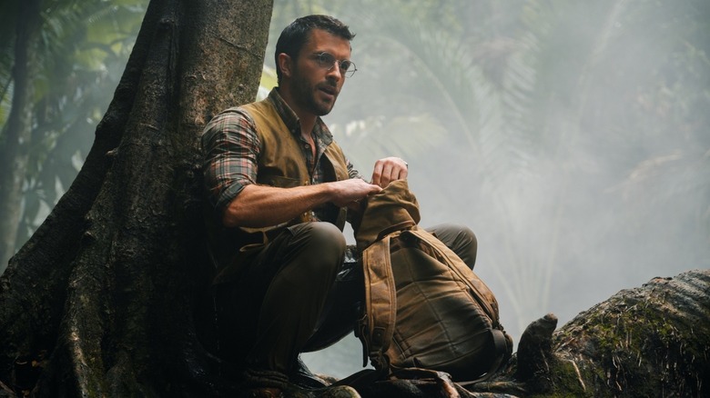 Dr. Henry Lomes sits on a tree with his bag in front of him on the ground in the birth of the global Jurassic