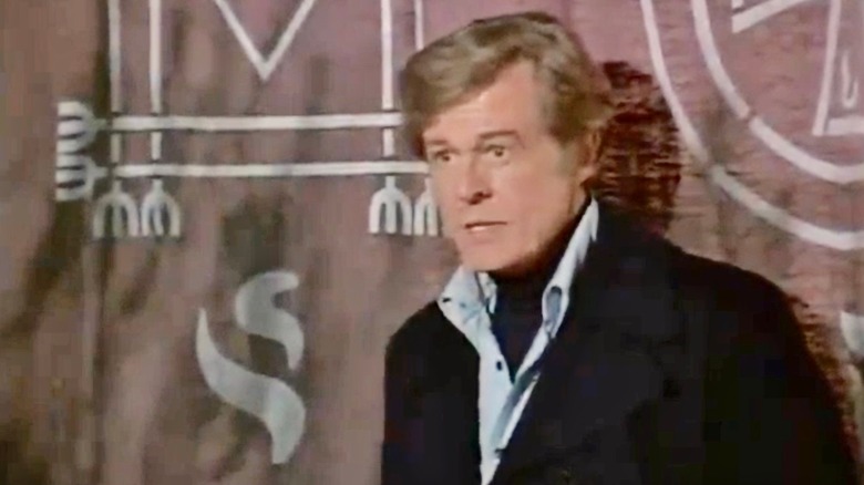 William Sebastian next to a Satanic tapestry in Spectre