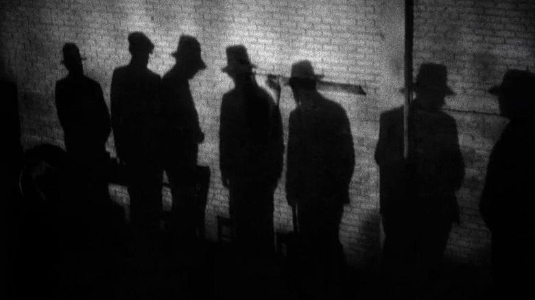 The shades of several people wearing hats on a brick wall in Scarvis (1932)
