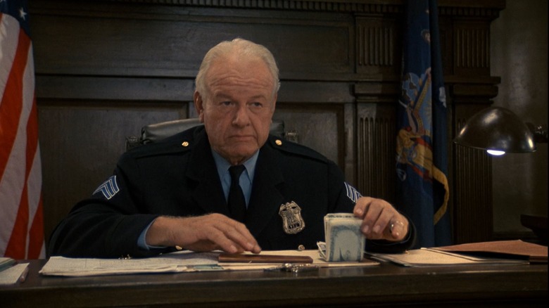 The grumpy desk sergeant holding some money in Johnny Dangerously